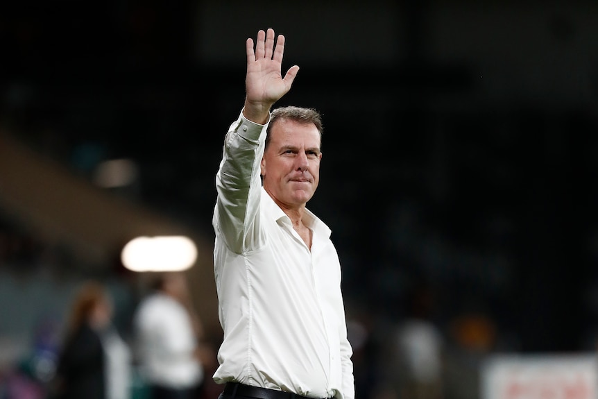 A man in a white shirt waves. 