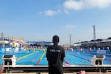 A woman in a black t-shirt with Malawi on the back of it looks out at a pool.