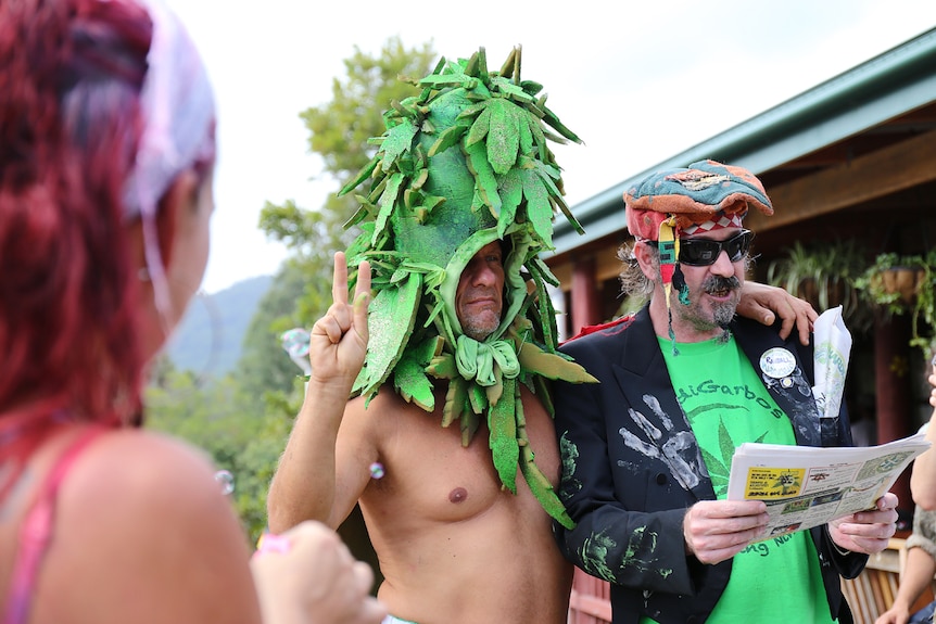 Man dressed in cannabis bud hat with arm around man in rastafarian cap