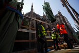 Workers secure a religious statue perched atop Paris' Notre Dame Cathedral.