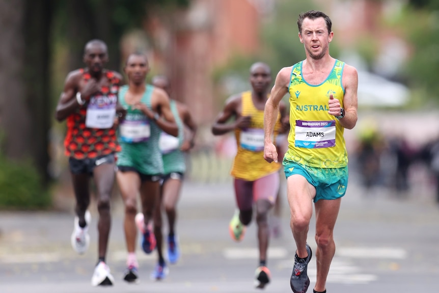 An Australian marathoner runs out in front, with a pack of athletes behind him. 