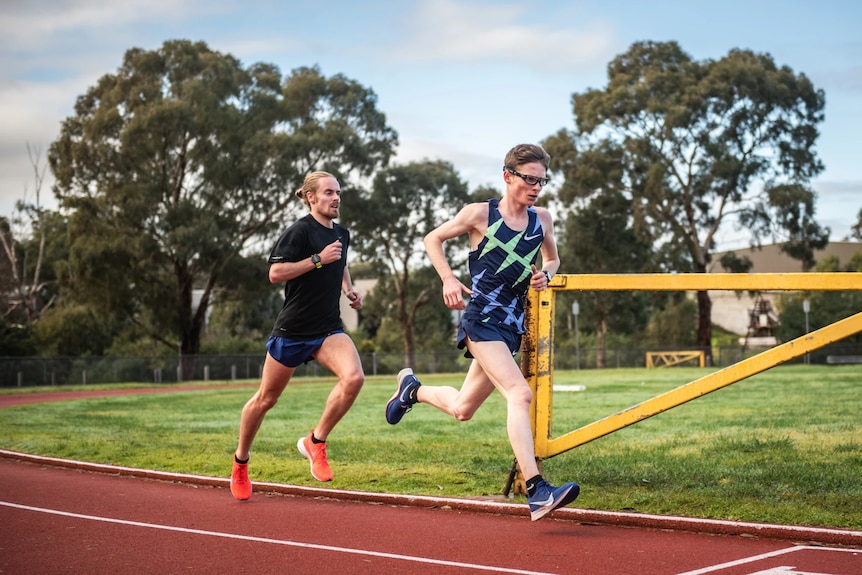 Jaryd Clifford leads his training partner Tim Logan as they run on an athletics track.