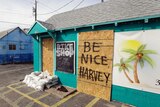 A sign reading "Be nice Harvey" is used to board up a business.