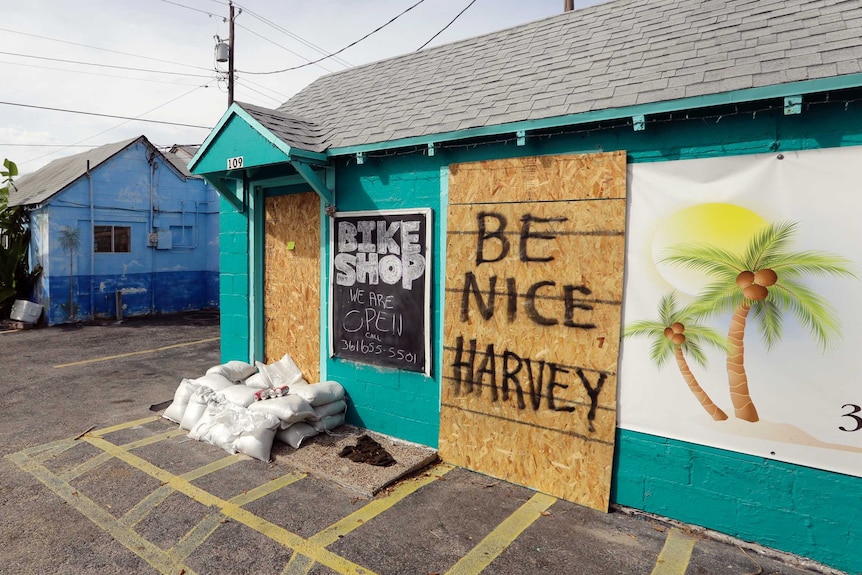 A sign reading "Be nice Harvey" is used to board up a business.