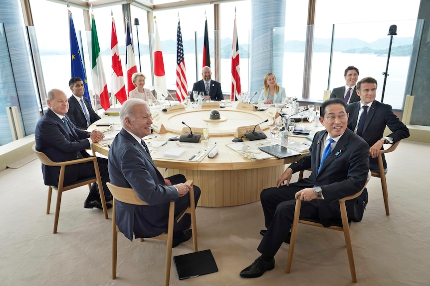 G7 nation leaders sit around a circular table and pose for photos.