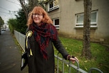 A woman wearing glasses stands alongside a fence while out campaigning.