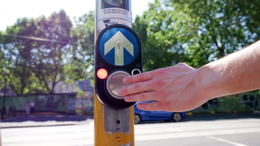 A photo of a pedestrian crossing button with a man's hand on it