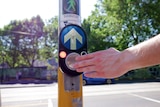 A photo of a pedestrian crossing button with a man's hand on it