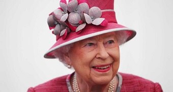 Queen Elizabeth II, wearing a pink floral hat, smiles for a photo.