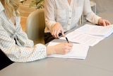 Two women in white button-down shirts look over papers