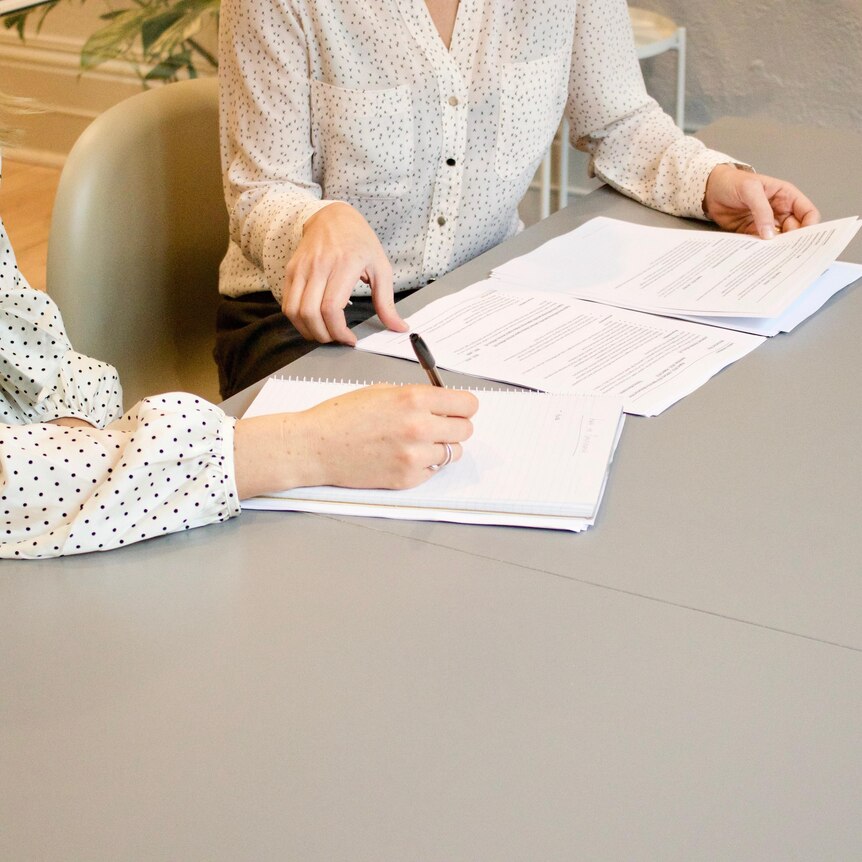 Two women in white button-down shirts look over papers