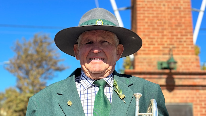 A older man in a green uniform holding a trumpet poses for a photo.
