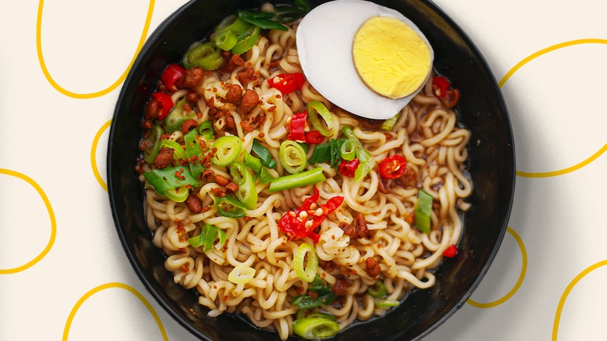 A bowl of instant noodles with half a boiled egg, chilli and chives added.