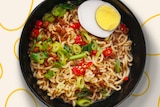 A bowl of instant noodles with half a boiled egg, chilli and chives added.