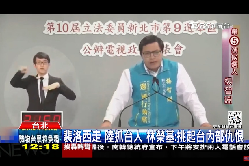 电视画面截屏显示一名穿着蓝色上衣的男子对着镜头发表演讲