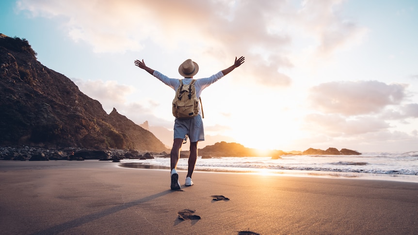 Young man arms outstretched by the sea at sunrise enjoying freedom and life.