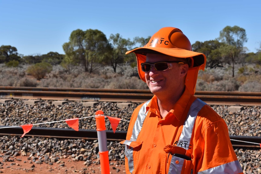 An older man wearing sunglasses and an orange hard hat.