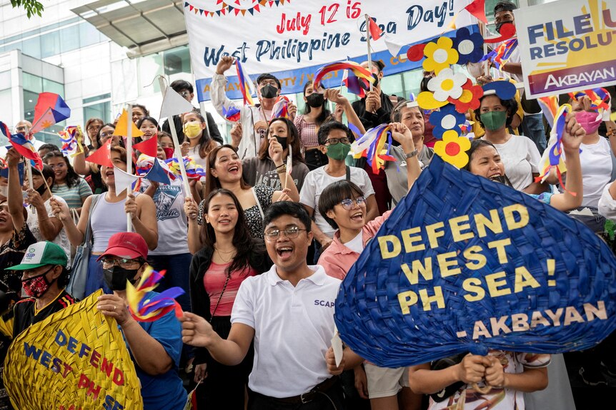 Crowd celebrates, holding up sign that says defend west ph sea 