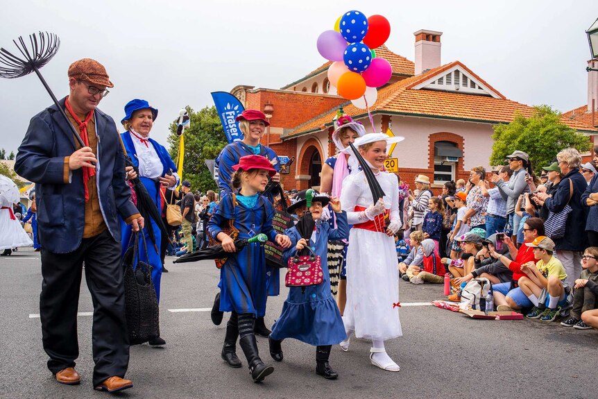 A group of people dressed as chimney sweeps, and Mary Poppins march in a parade.