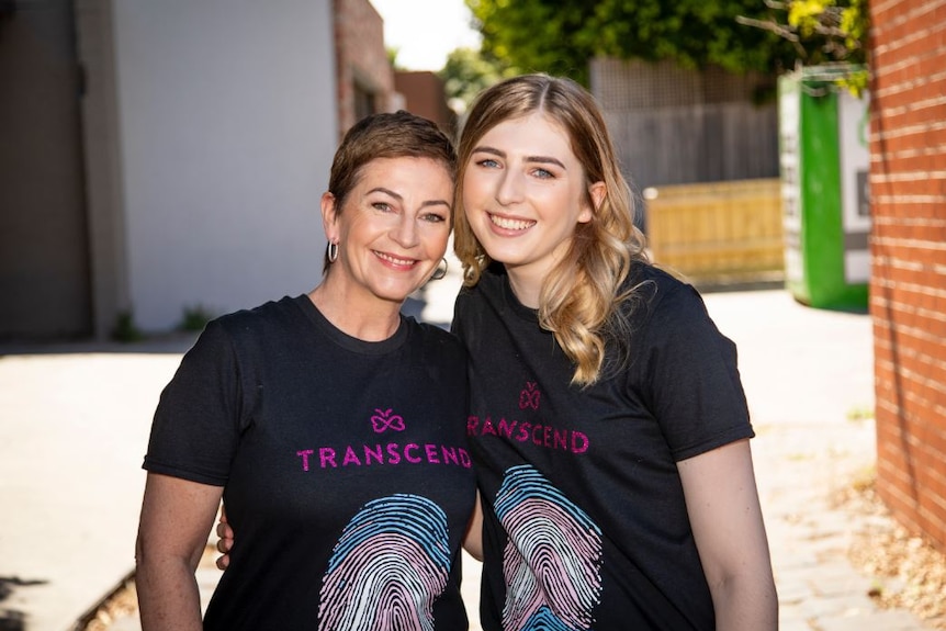 A mother and daughter stand together smiling and wearing black tshirts with the word "transcend" on it