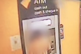 A man stands at a Commonwealth Bank ATM. He wears an orange shirt and jeans. His face is blurred.