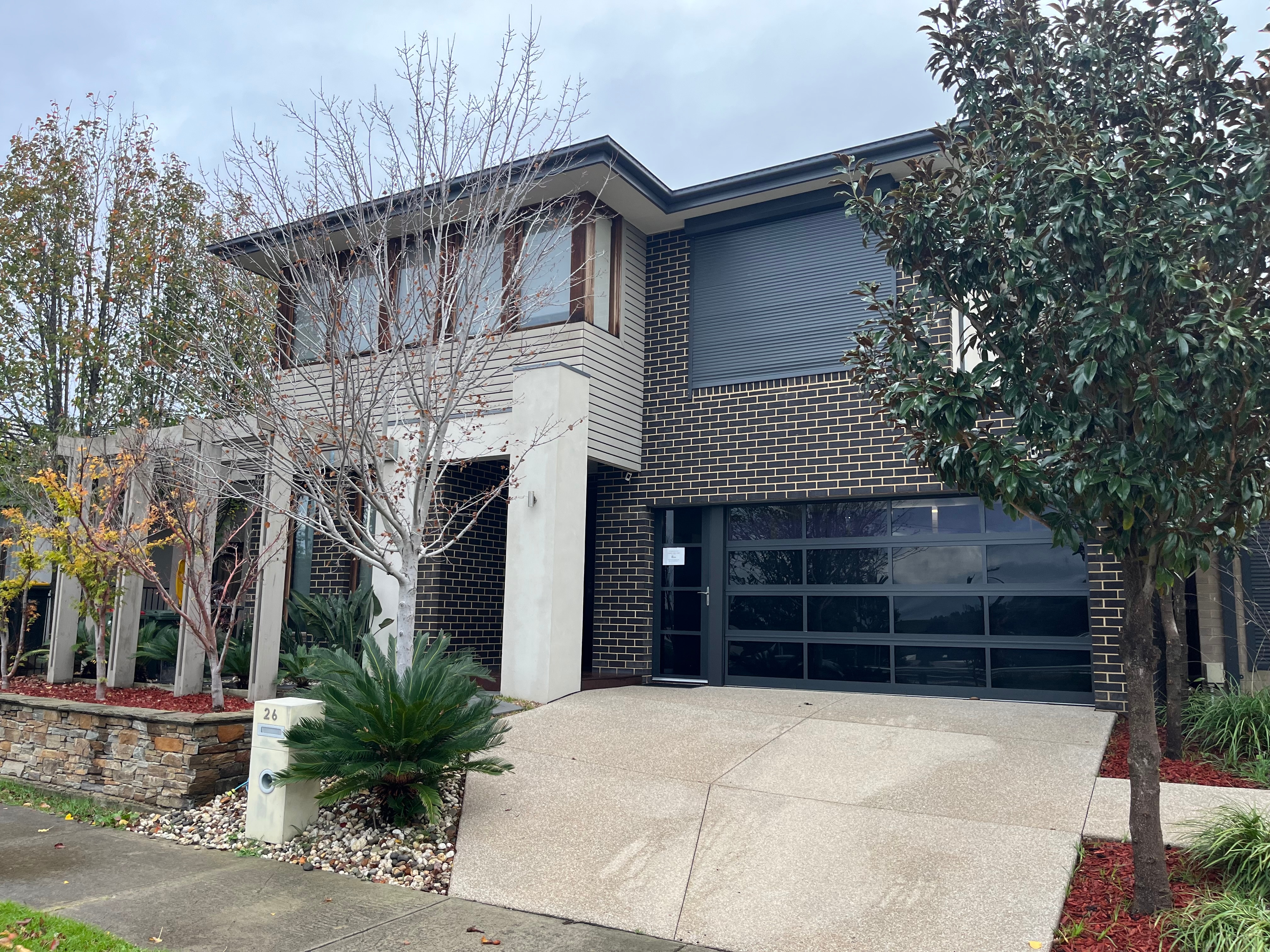 A black brick two storey residence with trees out front.