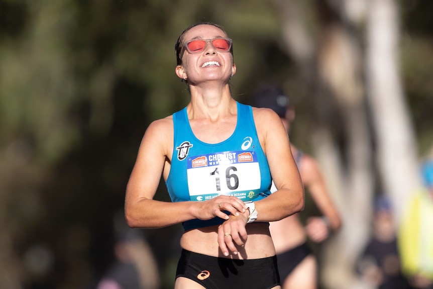 Australian race walker Jemima Montag stops her watch and smiles after crossing the finish line.