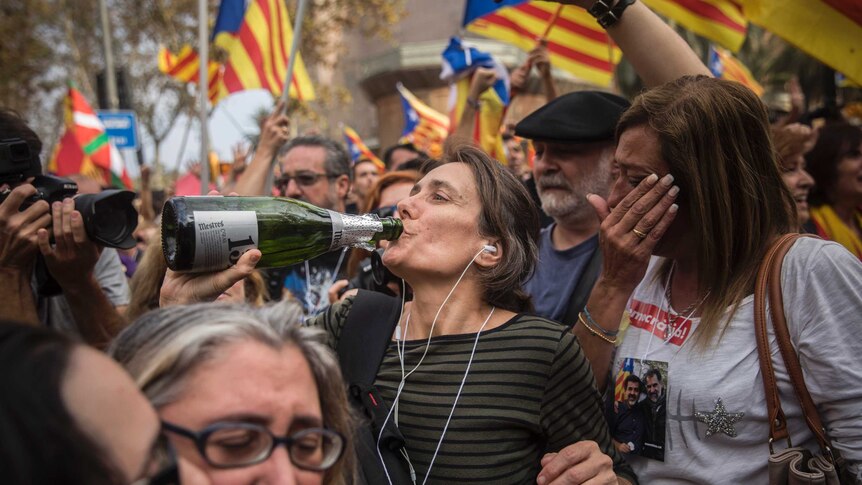 People wave "estelada" or pro independence flags in Barcelona. One woman drinks from what looks like a champagne bottle.
