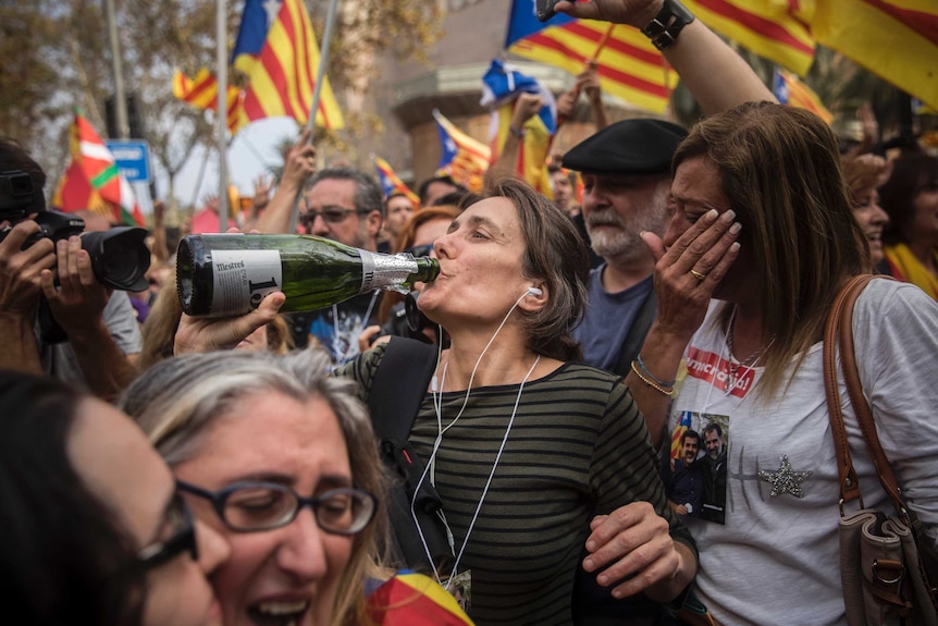 People wave "estelada" or pro independence flags in Barcelona. One woman drinks from what looks like a champagne bottle.