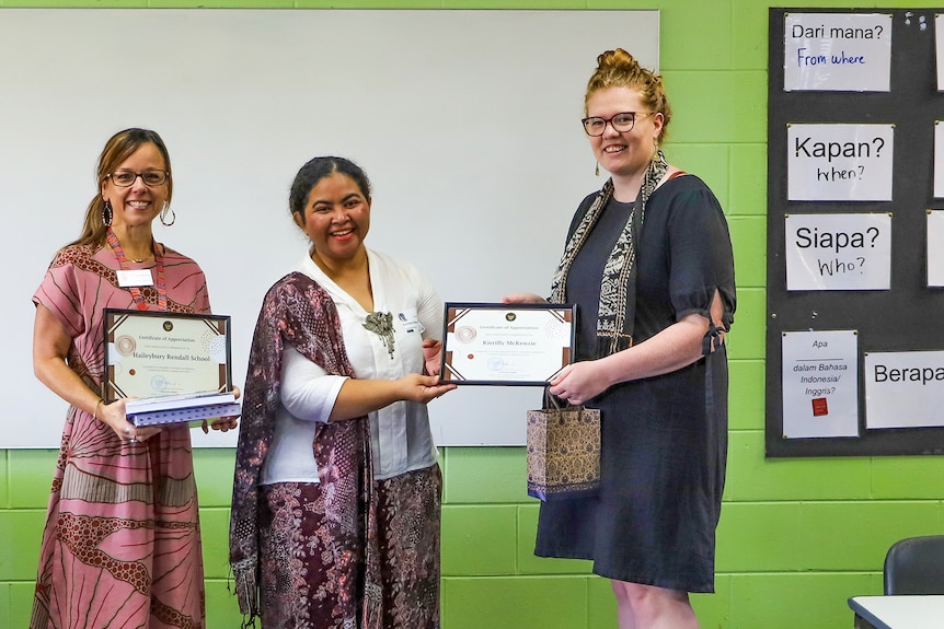 A smiling woman looks at the camera and hands a certificate to another woman