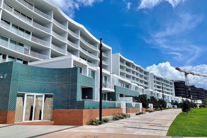 White and green apartment block with a footpath and green lawn out the front. 