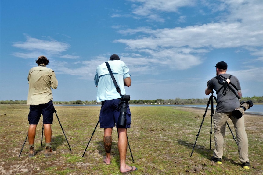 Three men with tripods and cameras looking for ducks on a lake.