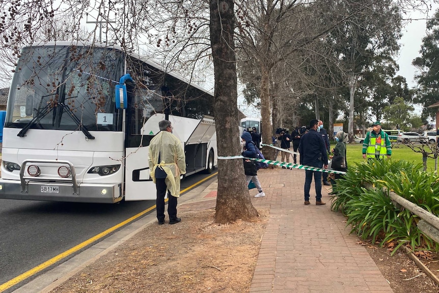 A bus next to a taped-off footpath with people standing around wearing face masks