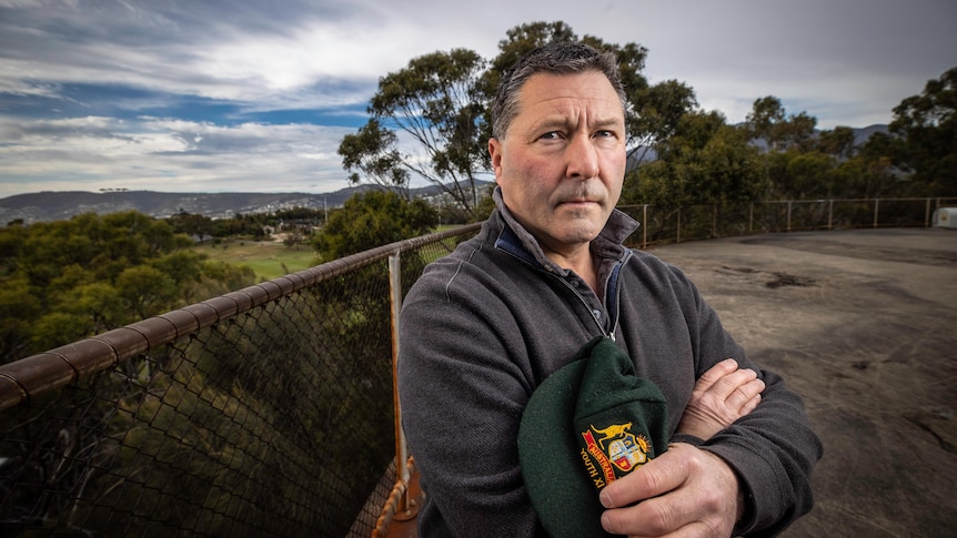 A man looks at the camera holding a green cap in his hand