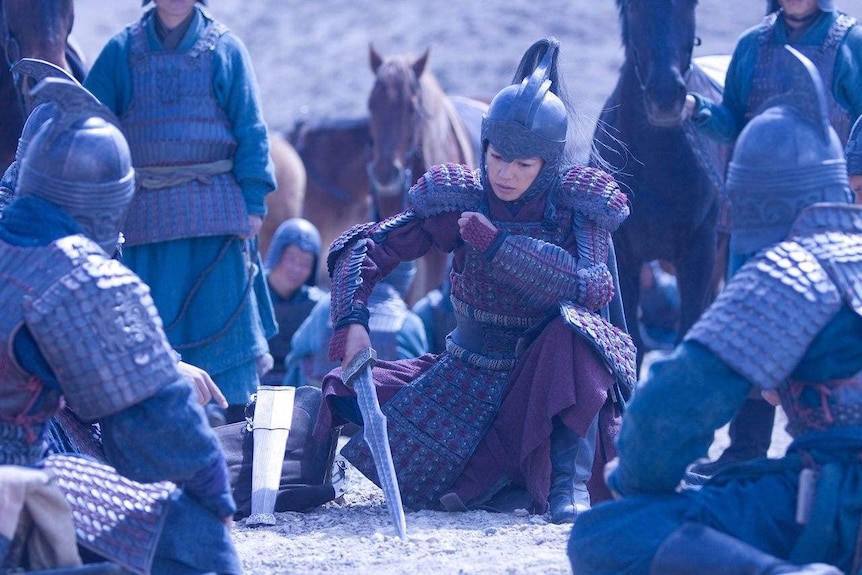 Wei Zhao dressed in armour holds a sword while kneeling. 