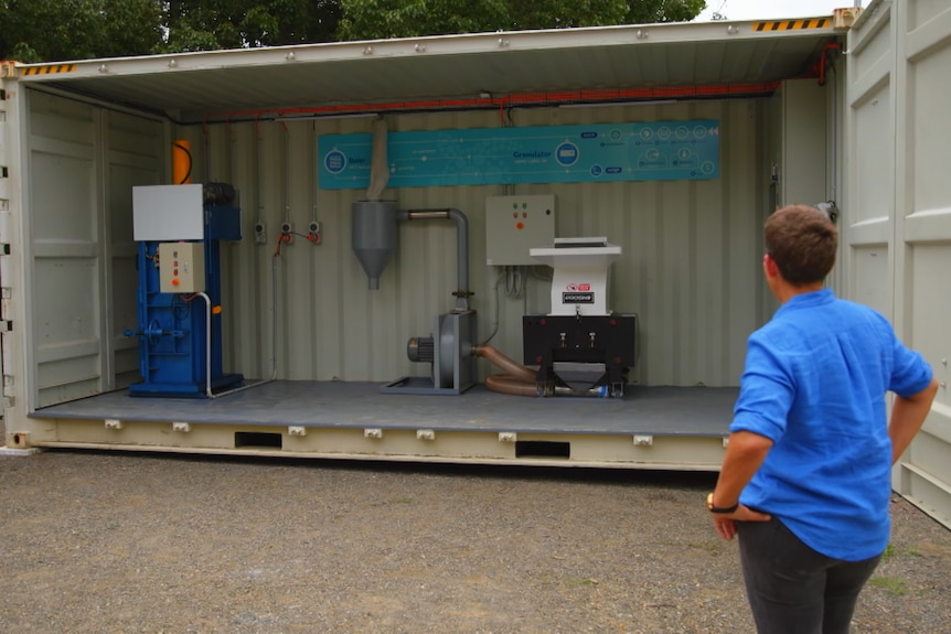 Shipping container with recycling machinery inside and woman looking inside. 