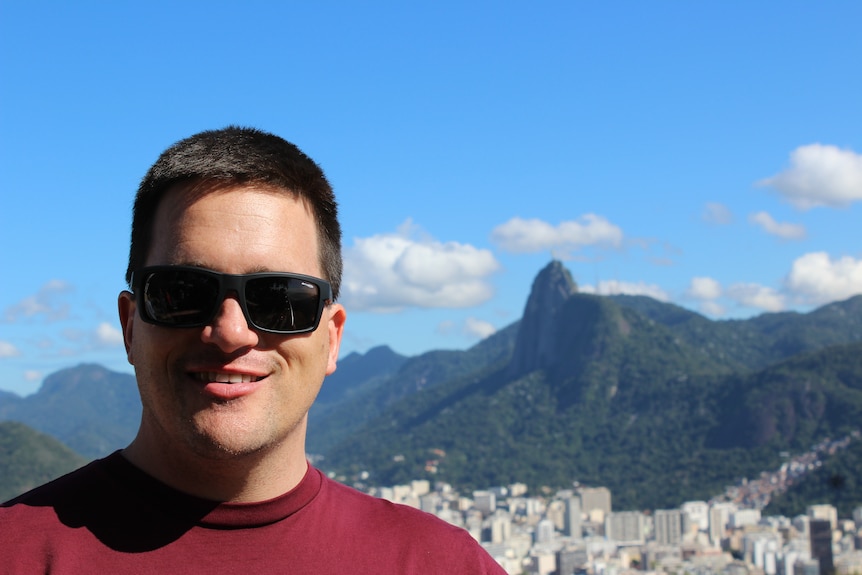 A man in sunglasses smiles with mountains behind him 