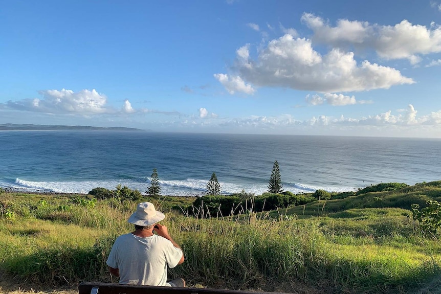 A lone man on a seat watches the waves roll by at Lennox Head.