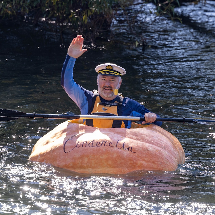 A man dressed as popeye sits in a hollowed out 400 kilo pumpkin waving as he paddles in a river