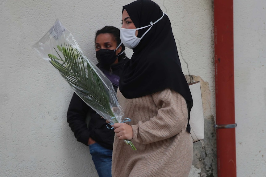 A woman wearing a headscarf carries flowers.