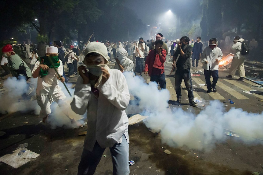 Muslim hardline protesters cover their faces as police fire tear gas