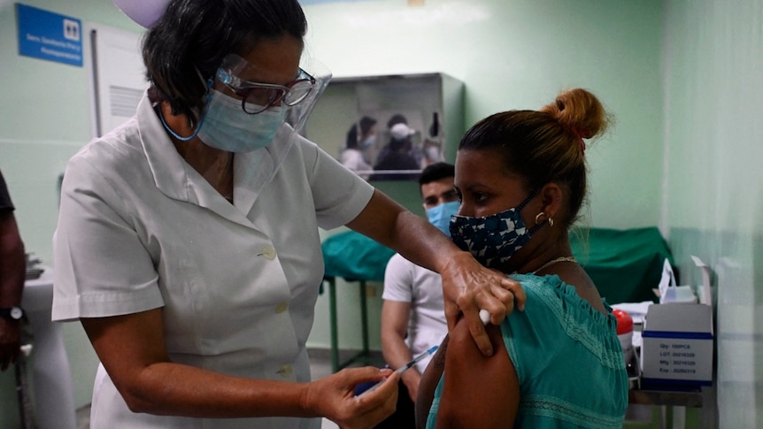 A nurse wearing a face shield and face mask vaccinates another health worker