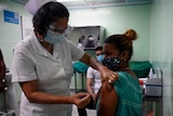 A nurse wearing a face shield and face mask vaccinates another health worker