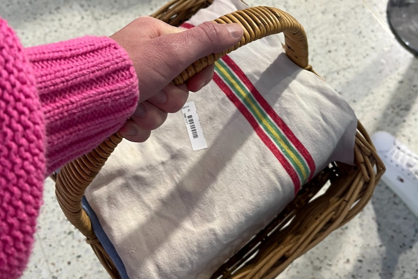 A hand holding a basket with a cake wrapped in a teatowel.