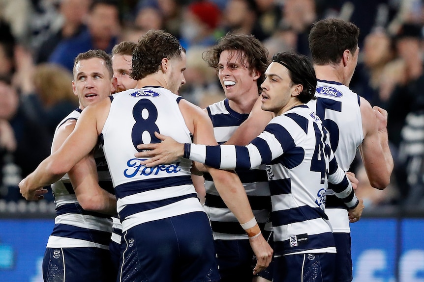 Geelong players celebrate by hugging and smiling