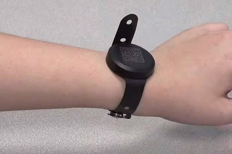 A wrist with a watch-like tracking wristband. On it's face is a QR code.
