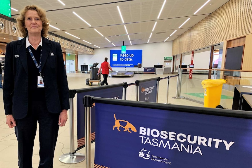 The director of biosecurity operations, Rae Burrows, stands inside the Hobart airport next to a biosecurity sign.