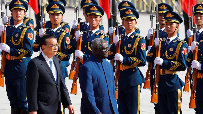 Manasseh Sogavare and Li Keqiang walk past an honour guard 