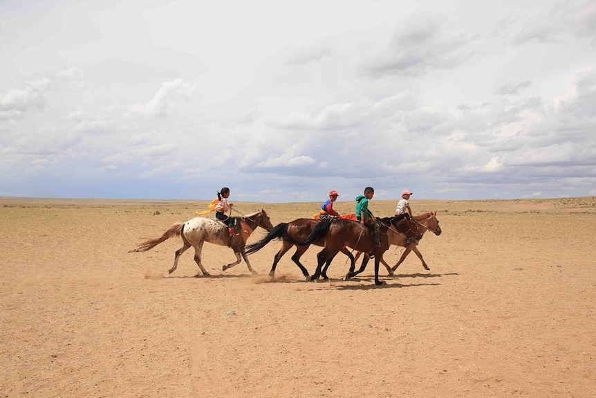 Four children sit on horseback and ride through the Gobi Desert.