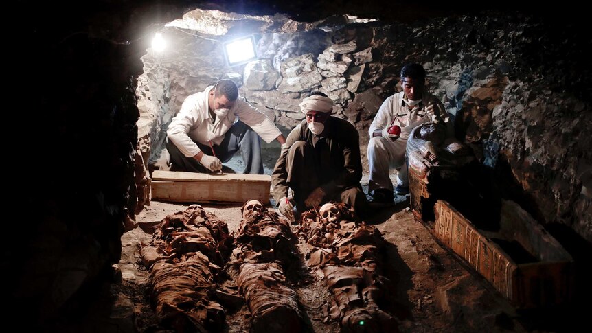 Archaeologists work on mummies inside a tomb